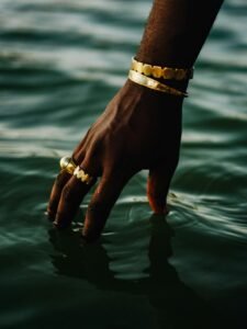 A hand adorned with gold jewelry gently touches calm water, creating a serene and luxurious atmosphere.